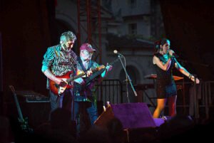 deux guitaristes et une chanteuse du groupe amazone en plein concert sous les feux de la rampe