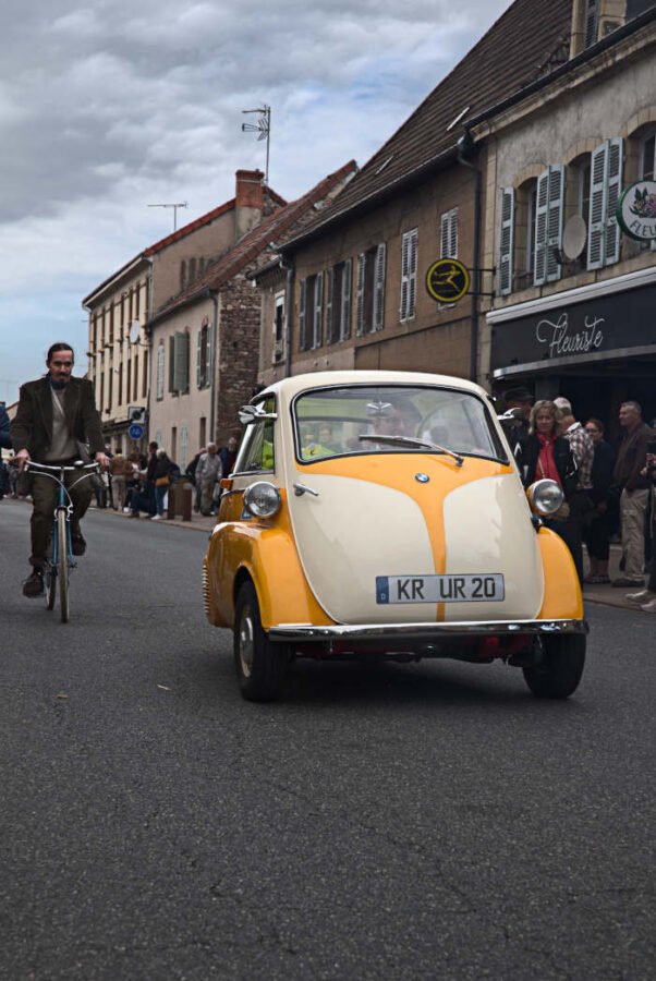 ancienne voiture a trois roues suivi par un cycliste 