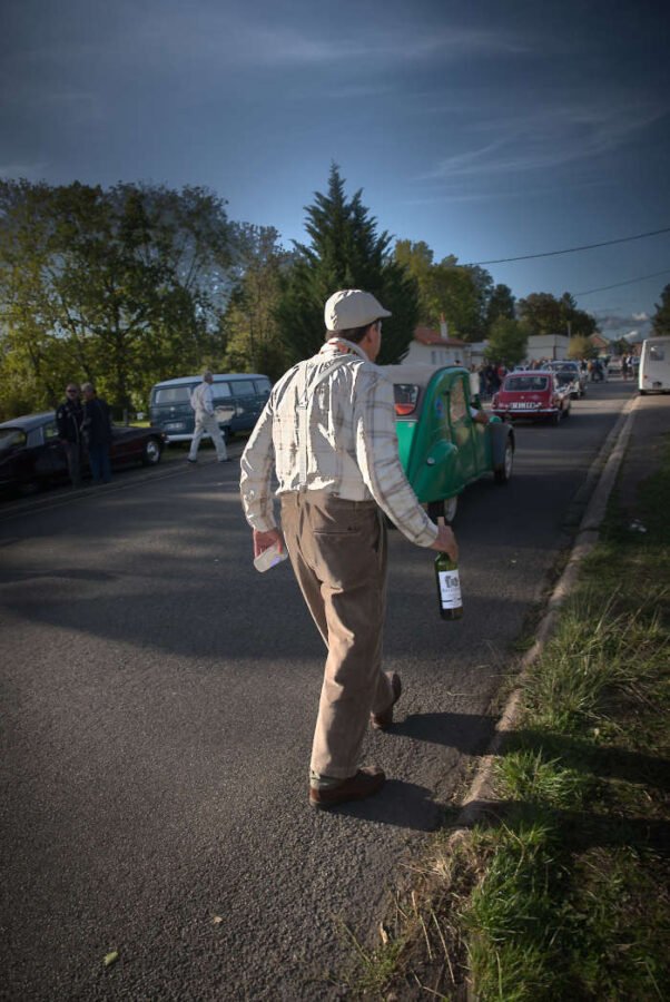 Un homme à la casquette marche le long de la route avec un litre de vin à la main